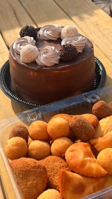 Torta de chocolate decorada com chantilly e docinhos, ao lado de uma bandeja de salgados