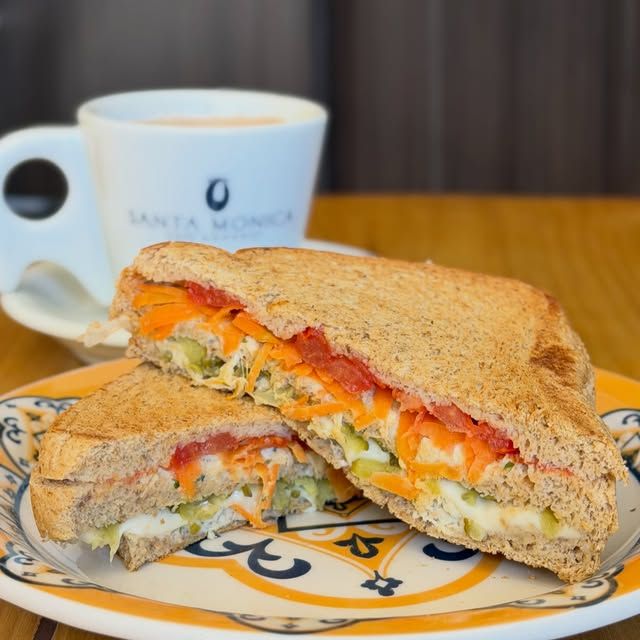 Sanduíche na torrada com cenoura, tomate e alface, ao lado de uma xícara de café